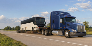 Commercial motorcoach on an RGN lowboy trailer pulled by a blue semi truck