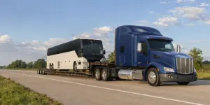 Commercial motorcoach on an RGN lowboy trailer pulled by a blue semi truck